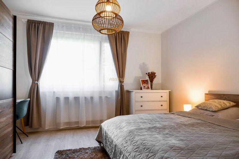 A bedroom in a 2-room apartment with decorative curtains and a wooden-patterned floor.