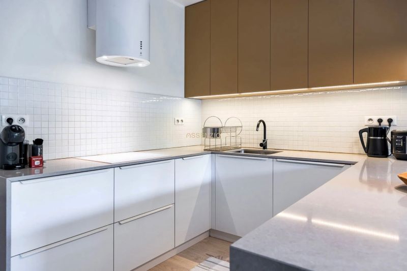 A kitchen in a two-room apartment with white cabinets, a black faucet, and appliances.