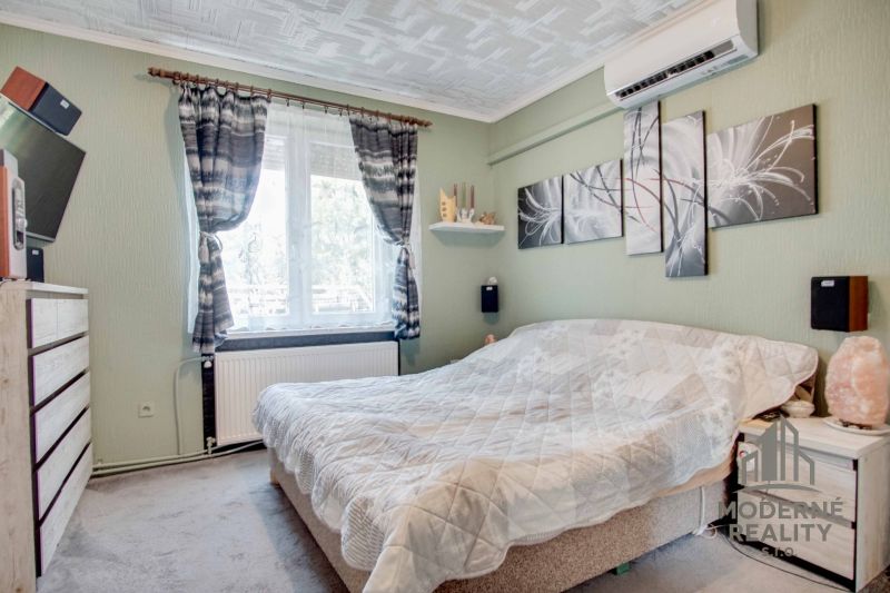 Bedroom in a 2-room apartment with a bed, paintings, and air conditioning on the wall.