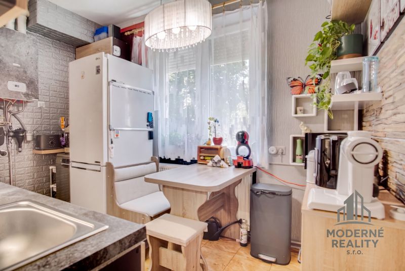A kitchen in a 2-room apartment with a dining area and appliances, wooden decor flooring.