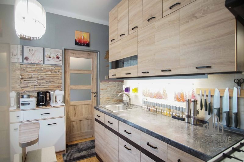 A kitchen in a 2-room apartment with a wooden decor floor and light furniture.