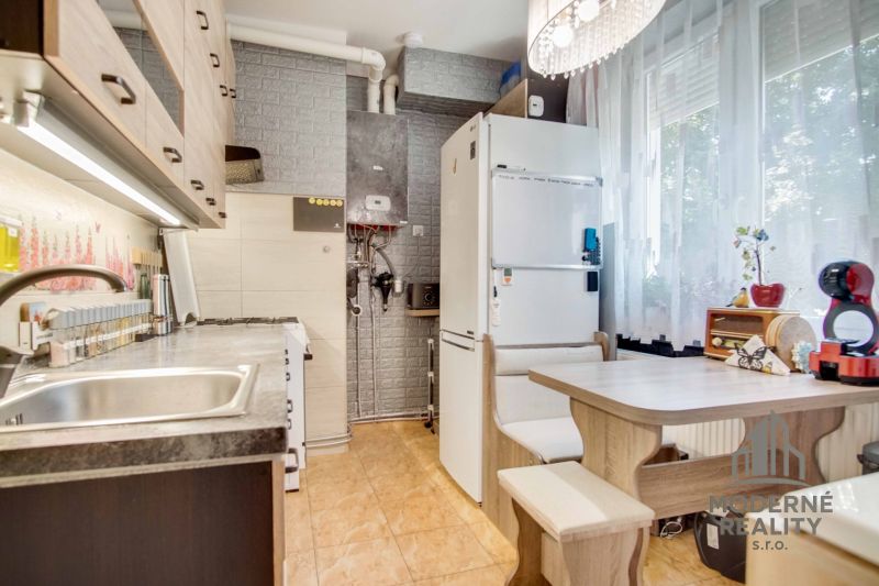 A kitchen in a 2-room apartment with appliances, a dining area, and a decorative brick wall.