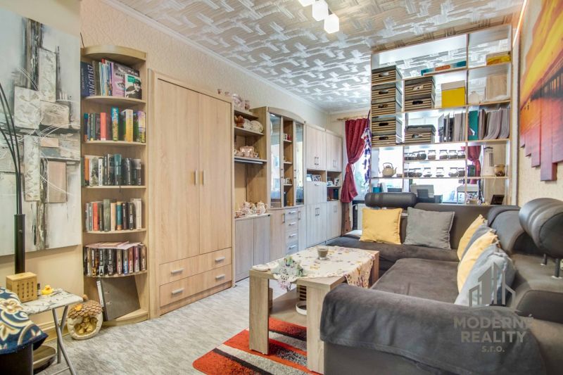 Living room with a bookshelf, sofa, and wooden decor flooring in a two-room apartment.