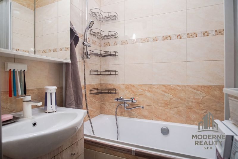 A bathroom in a 2-room apartment with a bathtub, shower, and shelves on the wall.