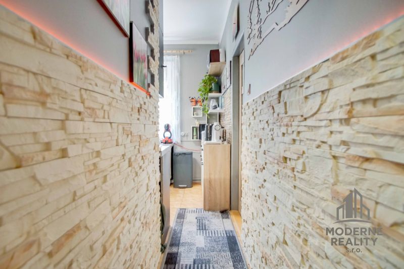 A narrow corridor with light brick cladding leading to the kitchen in a 2-room apartment.
