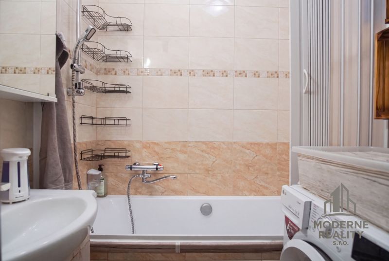 Bathroom with a bathtub and a washing machine in a 2-room apartment. Tiles with a beige decor.