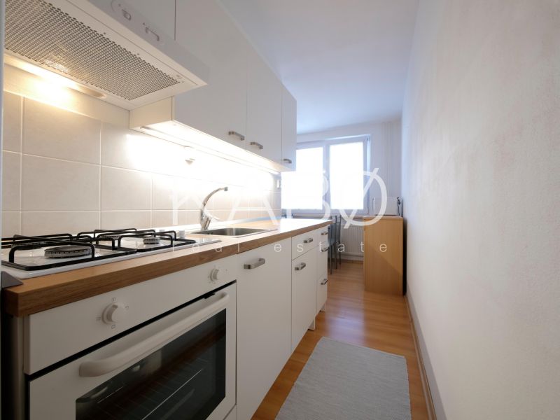A kitchen in a 2-room apartment with white cabinets and a wood-patterned floor.