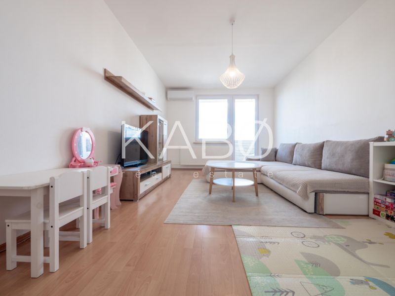 Living room in a two-room apartment with a wooden decor floor, a children's table, and a sofa.