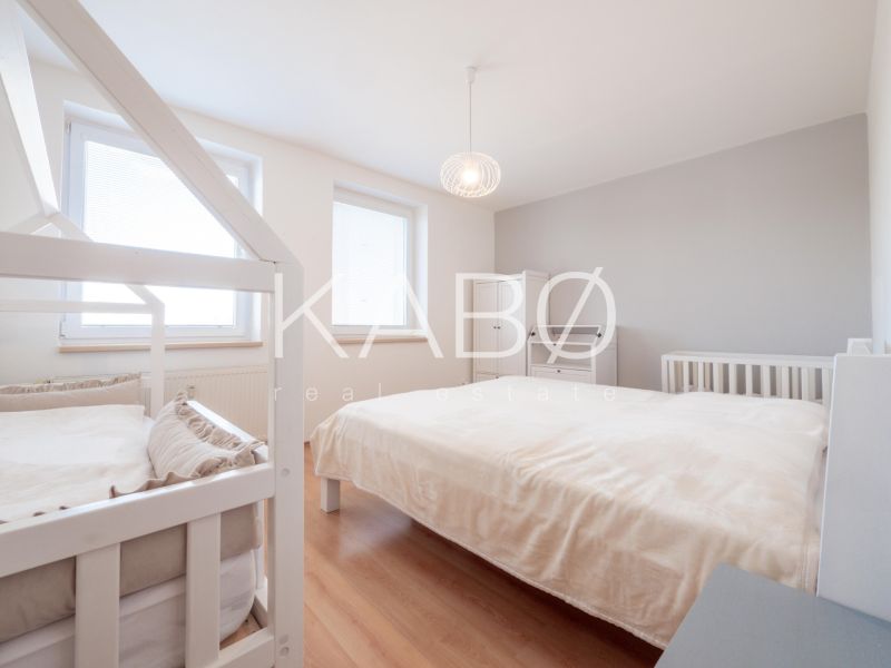 A bright bedroom in a two-room apartment with a bed, a baby crib, and a wooden decor floor.