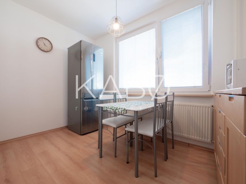 A kitchen with a wooden decor floor, dining area, and appliances in a two-room apartment.