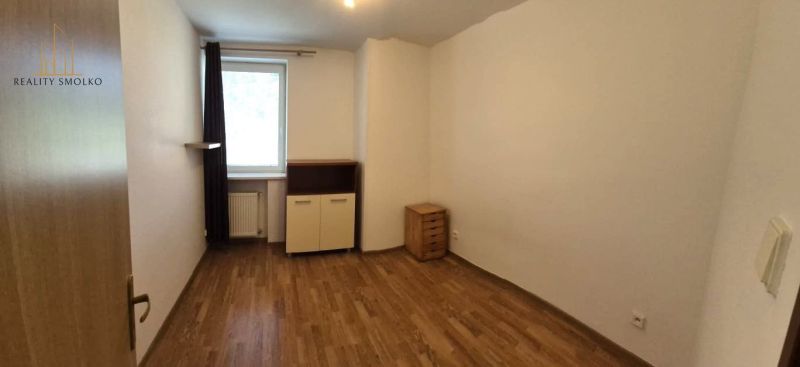 A room of a one-room apartment with a wooden decor floor, furniture, and white walls.