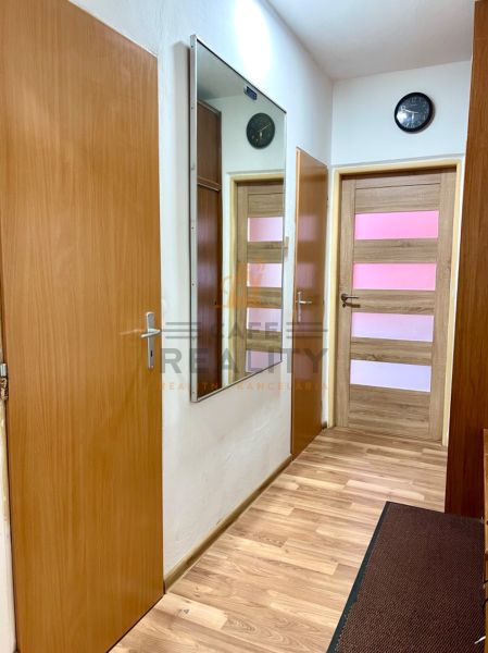 A hallway with a wooden decor floor in a 2-room apartment, a mirror and a clock on the wall.
