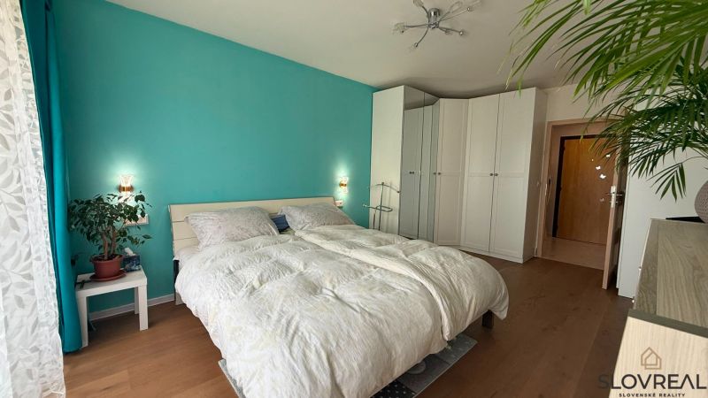 A bright bedroom with a turquoise wall, white wardrobes, and a wood-patterned floor.