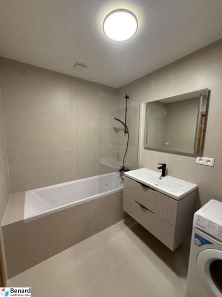 Bathroom in a 3-room apartment with a bathtub, sink, and washing machine, beige tiles.