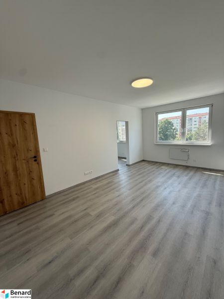 A room in a 3-room apartment with a wooden decor floor, white walls, and a window.