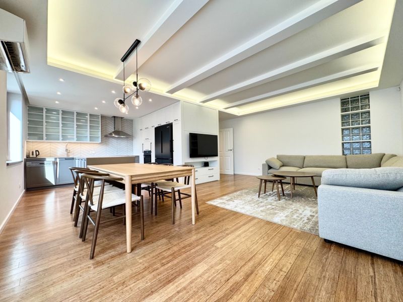 Living room in a 3-room apartment with a kitchen, dining table, and wooden decor flooring.