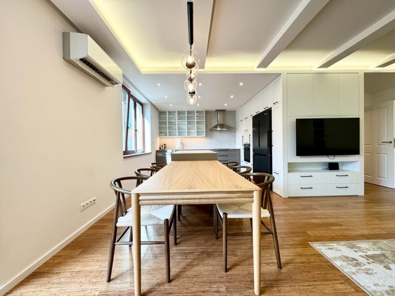A kitchen in a 3-room apartment with lighting, wood-decor flooring, and a dining table.