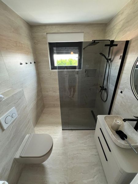 A bathroom in a 3-room apartment with a large shower and a wall-mounted toilet.