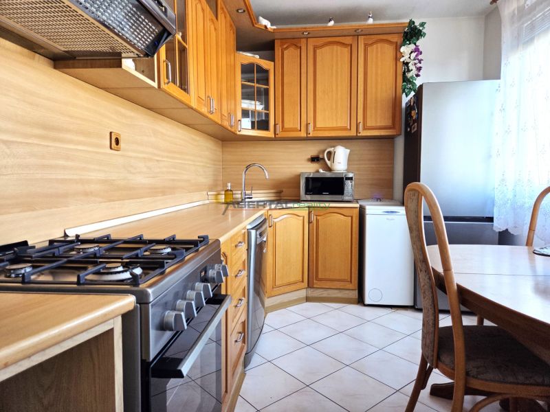 A kitchen in a 3-room apartment with wooden cabinets, a gas stove, and a dining table.