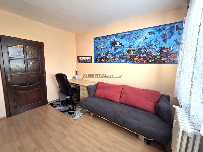 A room in a 3-room apartment with a wooden decor floor, a sofa, and a desk.