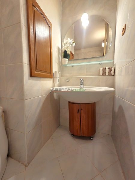A bathroom in a 3-room apartment with a mirror, a sink, and a cabinet with a wooden decor.