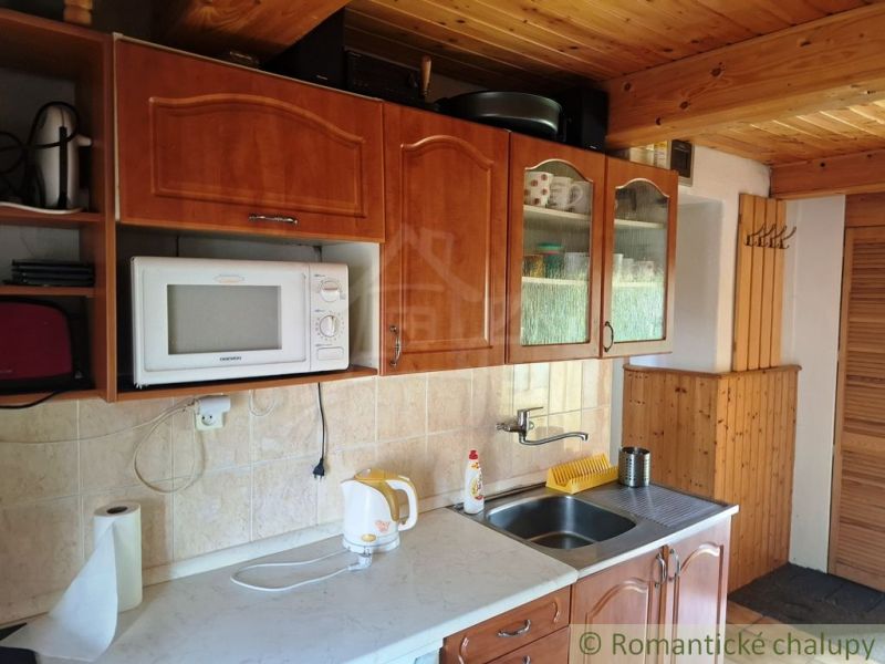 A kitchen with a wooden ceiling and cabinets, a microwave, a sink, a kettle.