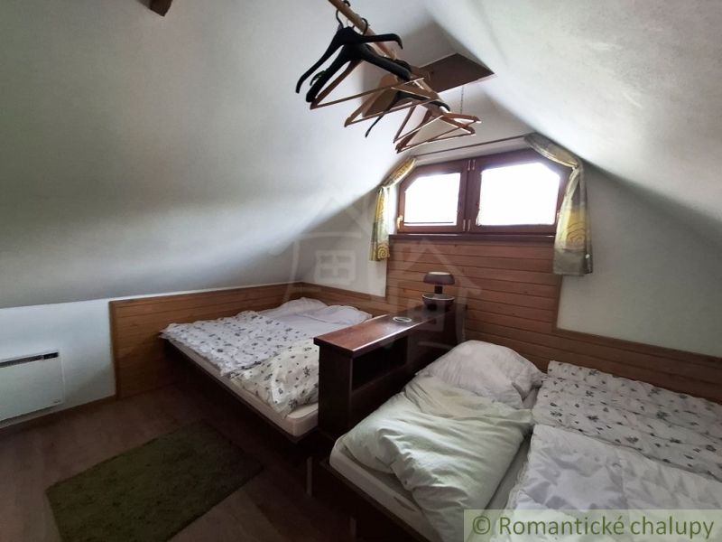 Attic with two beds, wooden decor floor, hangers, small window, low ceiling.