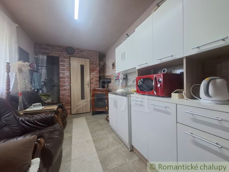 A kitchen in a cottage with white cabinets, a red microwave, and leather sofas.