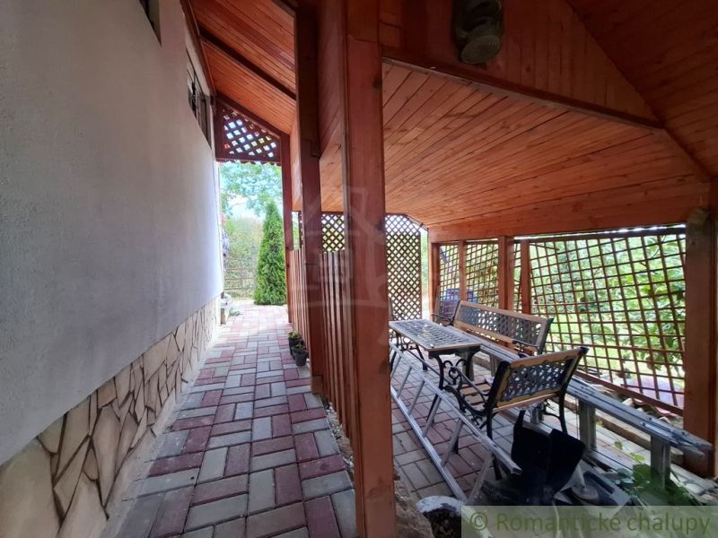 A terrace by the cottage in Gbelce with paving and garden seating under a wooden roof.