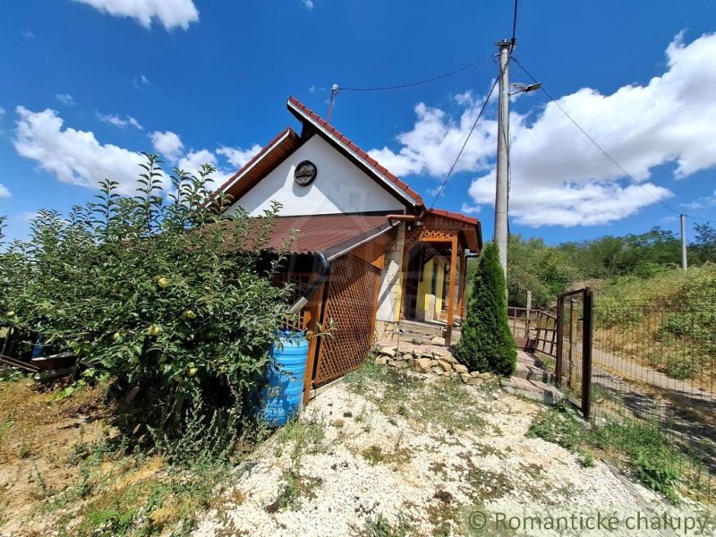 A cottage in Gbelce surrounded by greenery and trees under a blue sky.