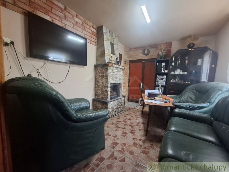 Stone fireplace and leather sofas in a cabin with a tile-style floor.
