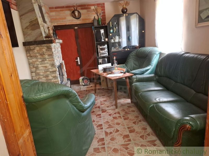 Interior of a cabin with a fireplace, leather sofa set, and a display case on a wooden-decor floor.