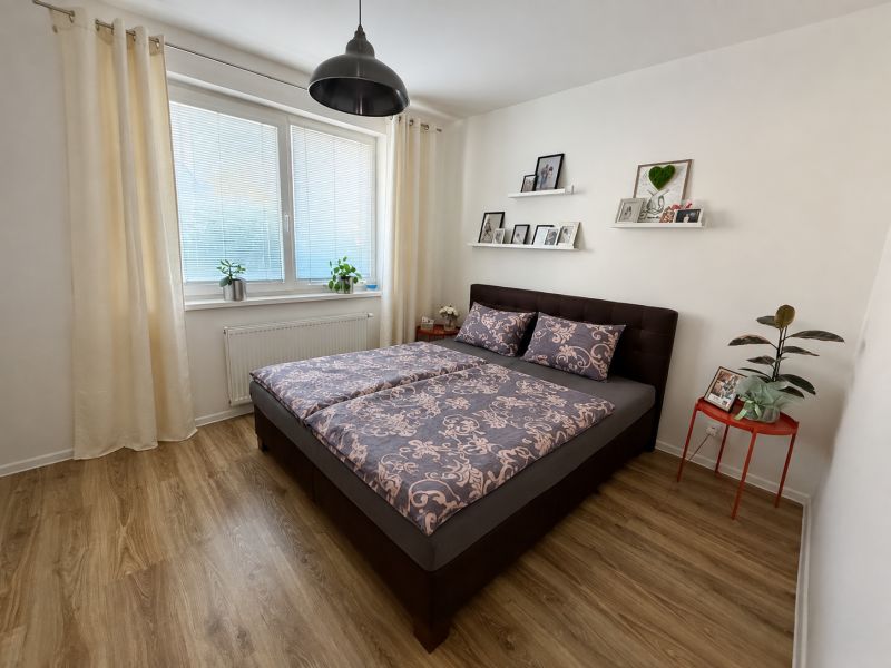A bedroom with a bed, wooden decor flooring, and decorations in a three-room apartment.