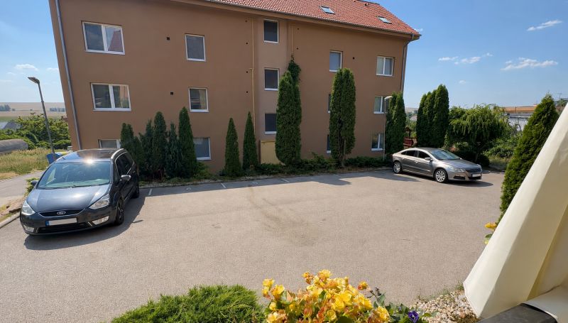 Parking lot in front of the apartment building in Veľký Lapáš with cars and greenery around.
