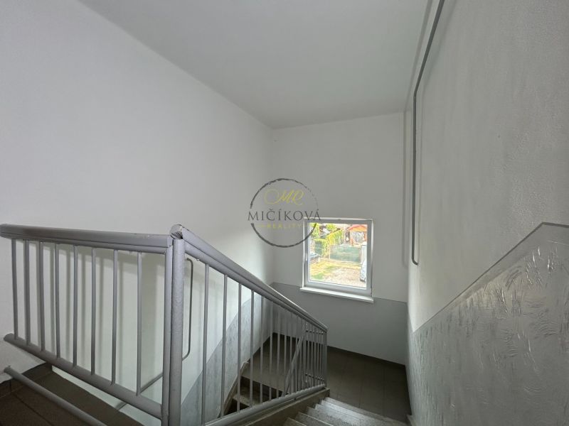 A staircase with a window in a 2-room apartment, the walls are white with a metal railing.