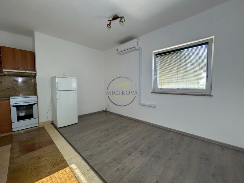 A kitchen in a 2-room apartment with a wooden decor floor, a white refrigerator, and a stove.