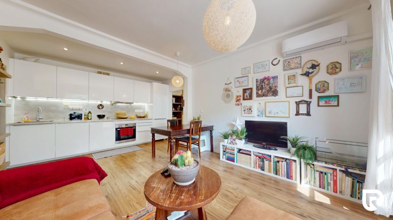 Living room of a three-room apartment with an open kitchen and a wooden decor floor.