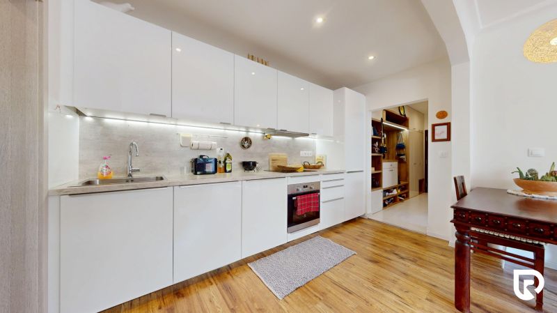 A kitchen in a 3-room apartment with a white kitchen unit and a wooden decor floor.
