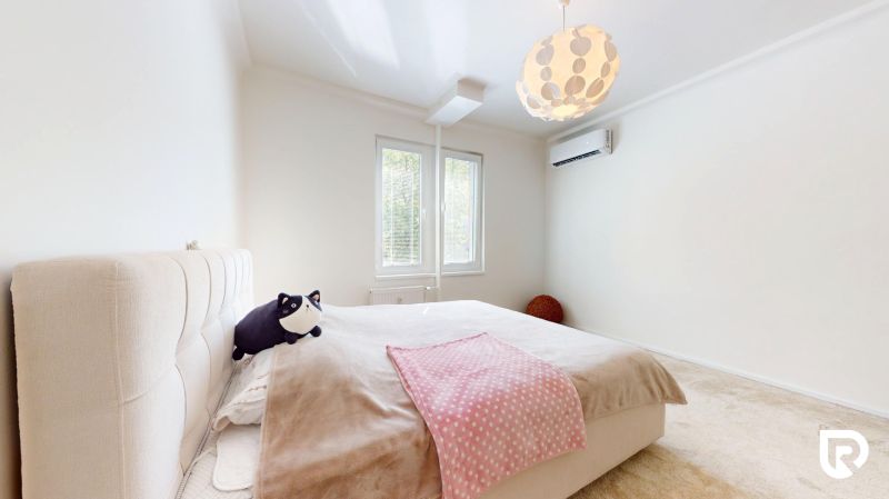 A bright bedroom with a large bed, two windows, and air conditioning in a 3-room apartment.