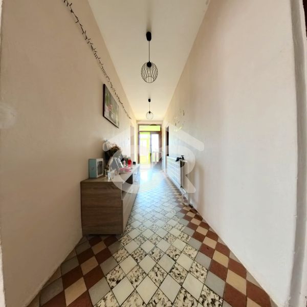 A hallway of a family house with a tiled floor, a chest of drawers, and ceiling lamps.