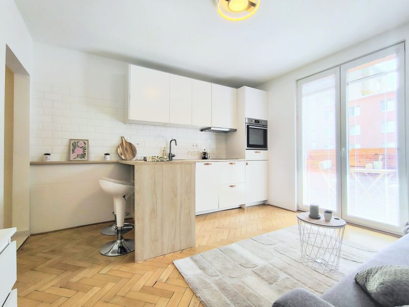 A kitchen in a 2-room apartment with white furniture, a floor with a wooden decor.