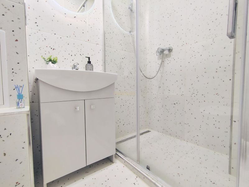 A bathroom with a sink, a shower corner, and terrazzo tiles in a 2-room apartment.