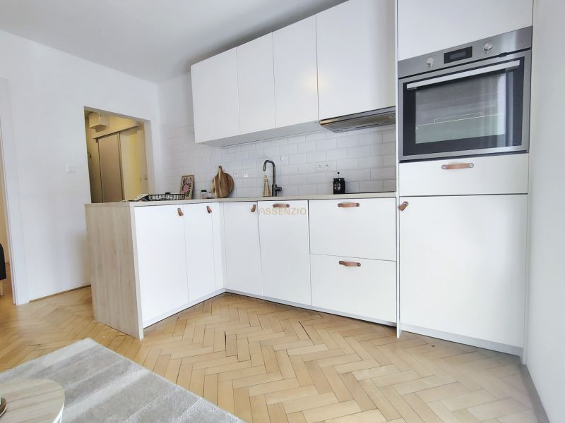 A kitchen in a 2-room apartment with light cabinets and a wooden decor floor.