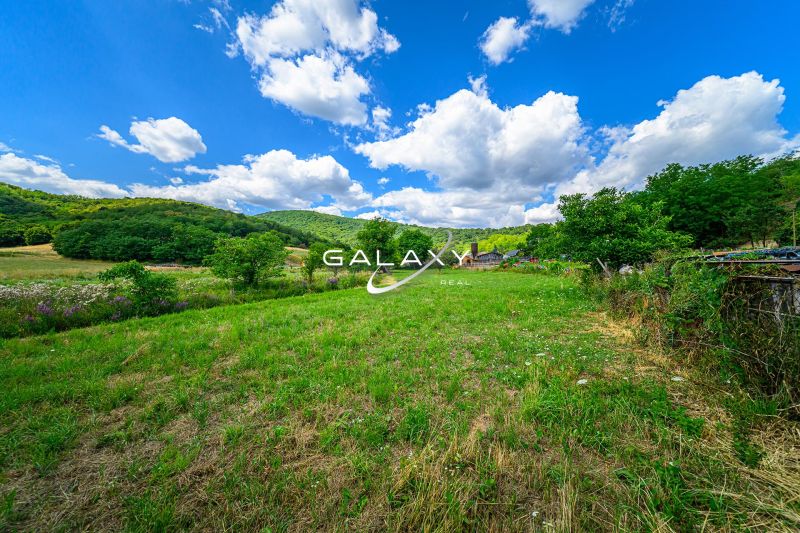 A plot of land surrounded by greenery near Hajnáčka with a clear blue sky and white clouds.