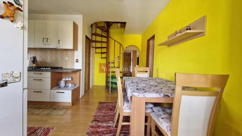 A kitchen in a 2-room apartment with a wooden decor floor and spiral stairs.