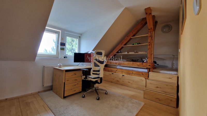 An attic office with a desk, chair, and wooden decor flooring in a 2-room apartment.