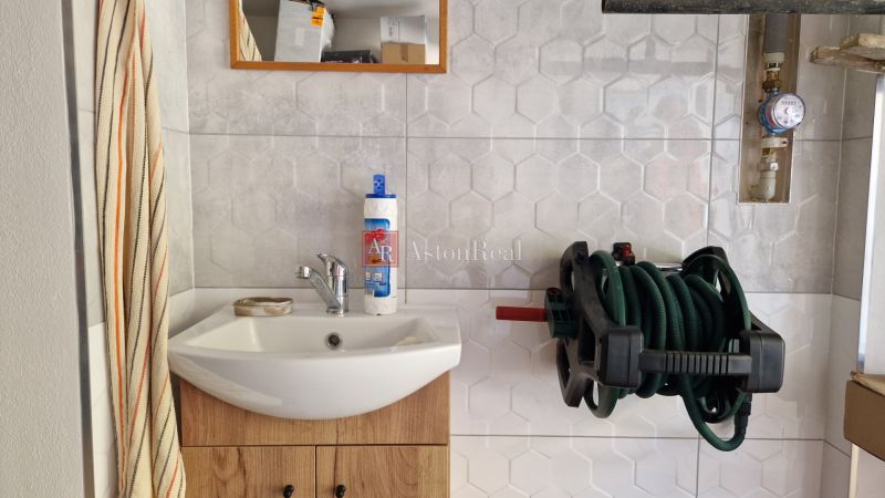 Bathroom in a 2-room apartment with a sink, mirror, and wall-mounted hose holder.
