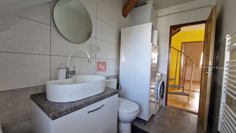 A bathroom in a 2-room apartment with a sink, a round mirror, and a washing machine.