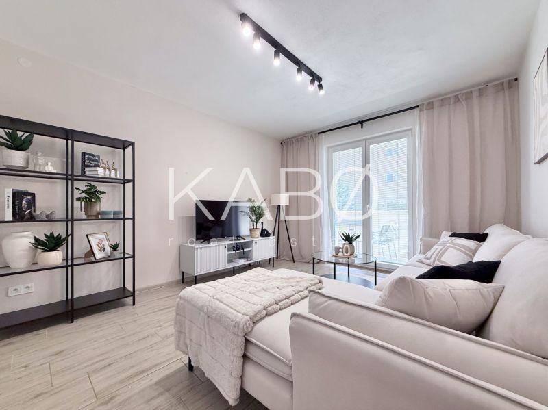 A bright living room in a two-room apartment with a shelving unit and a sofa, wooden decor flooring.