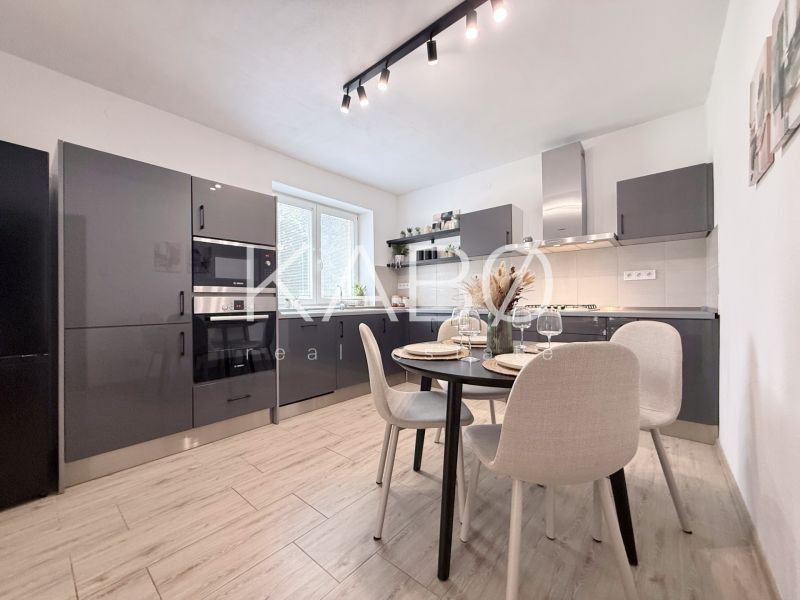 A kitchen with dark cabinets and a dining table in a two-room apartment with a wooden decor floor.